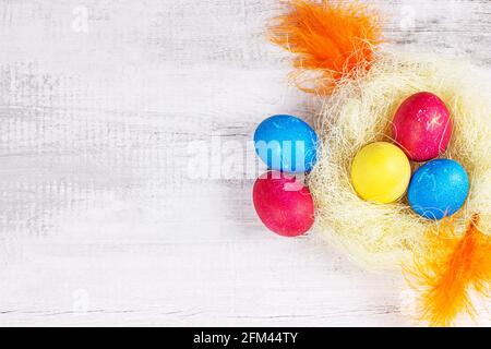 Top view flat lay colorful painted Easter eggs decorations in the nest with copy space on light wooden background. Stock Photo