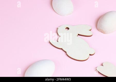 Funny wooden Easter Bunny with eggs as symbols of a holiday with copy space on light pink background. Stock Photo