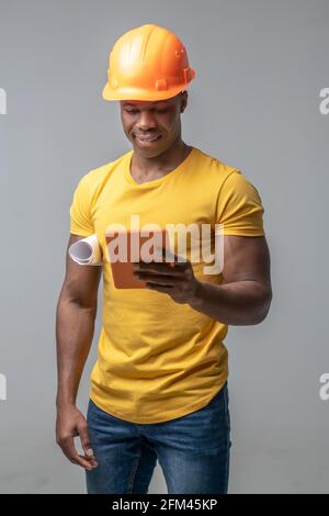 Dark-skinned construction worker in helmet with tablet Stock Photo