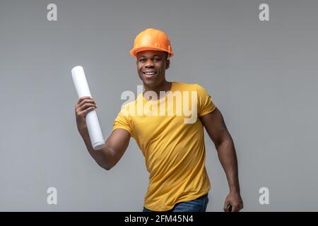 Cheerful man in construction helmet with roll of paper Stock Photo