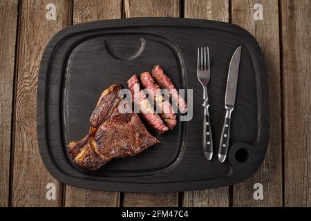 Top view of sliced veal entrecote on black board with cutlery Stock Photo