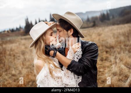 Portrait of handsome man kissing adorable woman in white bridal dress. Gorgeous stylish marriage couple hugging at the field, having wedding Stock Photo