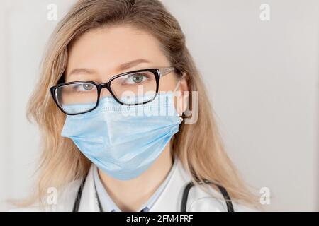 Portrait of woman doctor in blue mask and eyeglasses, while coronavirus pandemic. Caucasian female in medical uniform is looking at the camera, remind Stock Photo