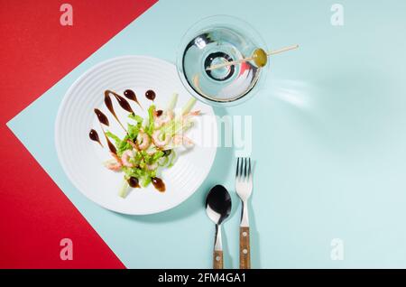 Elegant food in trend color style - green salad with shrimps and cocktail decorated green olive with shadow in hard light on red and minty background, Stock Photo