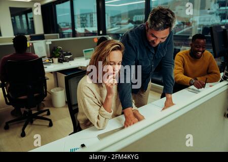 Male and female designers working on research report referencing essay on laptop standing in office block Stock Photo