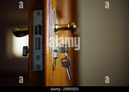 Closeup opened brown wooden door with handle and keys. Stock Photo