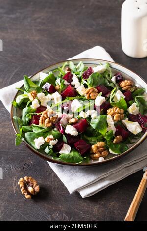 Beet or beetroot salad with fresh arugula, soft cheese and walnuts on plate, dressing and spices on dark wooden background, copy space, top view/ Stock Photo