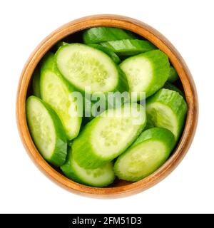 Slices of snack cucumbers, in a wooden bowl. Heap of diagonally cut fresh, small, young and whole cucumber fruits. Cucumis sativus, a vegetable. Stock Photo