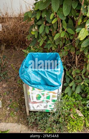 Trash can with blue plastic foil and bush Stock Photo