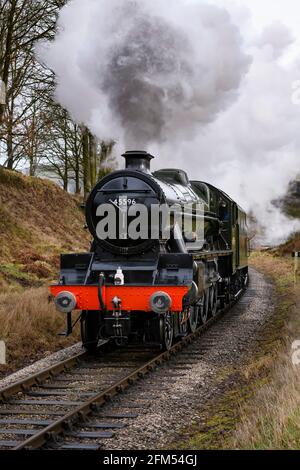 Historic steam train (loco) coming round bend in track, puffing smoke clouds travelling on scenic rural heritage railway - KWVR, Yorkshire England UK. Stock Photo
