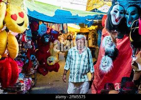 Mysore, Karnataka, India - January 2019: An Indian man walking through a street market past shops selling colorful and scary masks. Stock Photo