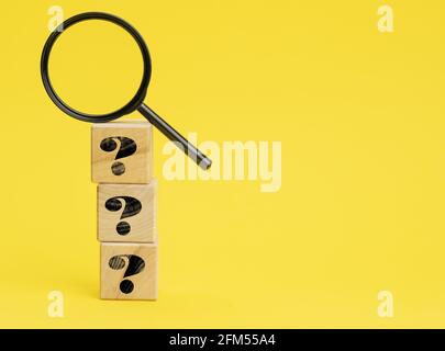 wooden cubes with question marks and a magnifying glass on a yellow background. The concept of finding answers to unknown questions, solving a problem Stock Photo