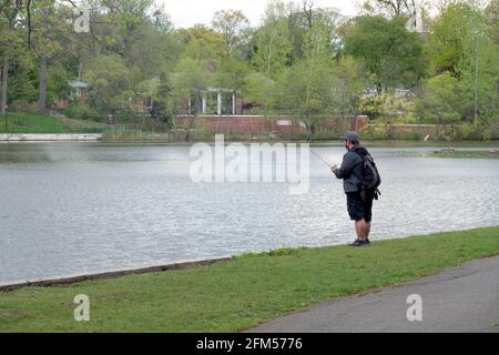 An Asian American man wearing a backpack fishes in the lake at Kissena Park in Flushing, Queens, New York City. Stock Photo