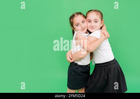Schoolgirls hug each other on green background. School friendship. Best friends Stock Photo