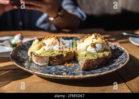 Two pieces of toasted rye bread with mashed avocado, poached eggs and sauce. Sandwiches with egg, avocado and sauce. Stock Photo