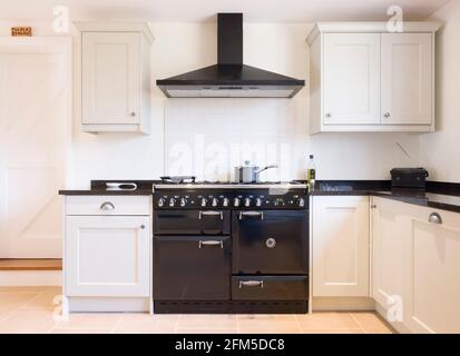 Modern modular kitchen interior in black and off white, with range cooker and chimney extractor hood. UK painted wood farmhouse kitchen design. Stock Photo