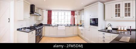 Modular painted wood kitchen, panoramic of modern UK farmhouse kitchen with neutral units and black granite worktops Stock Photo