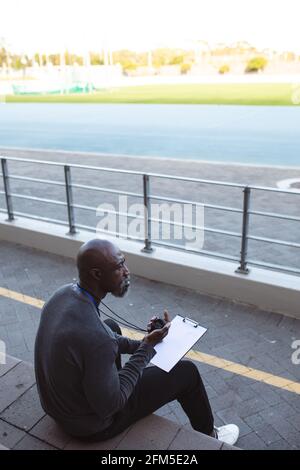 African american male coach with stopwatch measuring time while sitting on the seats in the stadium Stock Photo