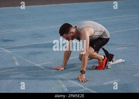 Caucasian male athlete with prosthetic leg in starting position for running on the track Stock Photo