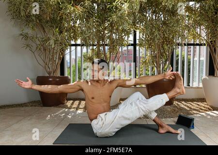 Smiling young Brazilian man taking online yoga class and holding his big toe. Stock Photo