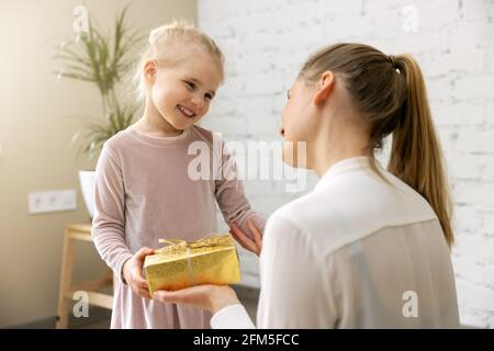 smiling daughter giving gift box to her mom at home. birthday or mothers day concept Stock Photo