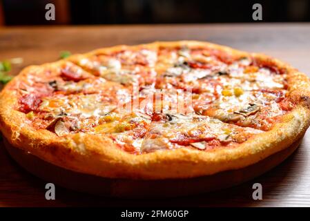 Close up acute view of Italian pizza with ham, cheese and mushrooms on wooden cutting board places on empty table. Stock Photo