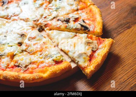 Close up view of italian pizza placed on wooden table while cut out pizza slice is sticking out of wooden plate. Stock Photo