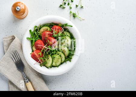 Fresh salad with tomato, cucumber, vegetables, microgreen radishes in white plate on grey stone background. View from above. Concept vegan and healthy