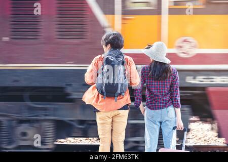 Couple of stylish tourists with backpacks and going into train at outdoor metro station, Asian couple traveling train station vintage style concept, i Stock Photo