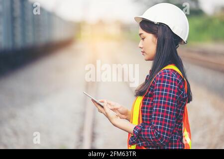 Portrait of beautiful woman engineering using tablet with wear hardhat in front of train garage. Stock Photo