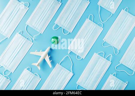 A white plane surrounded by protective masks on a blue background with a green and red dot as the destination. The concept of allowing and banning air Stock Photo