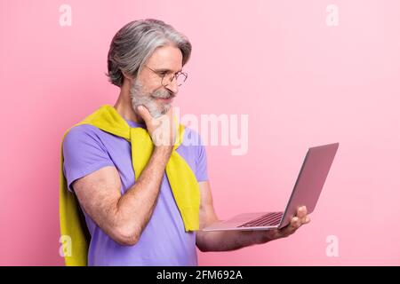 Profile side view portrait of attractive focused minded skilled gray-haired man using laptop isolated on pink pastel color background Stock Photo