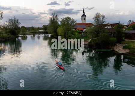 Woman in red kayak kayaking on the river Krka in Slovenia, with the sourounding small town Kostanjevica Stock Photo