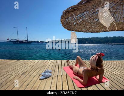 Face mask hanging on a straw beach umbrella. woman sunbathing sitting ...