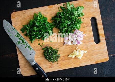 Chopped Herbs on a Bamboo Cutting Board: Chopped parsley, cilantro, oregano, shallots, and garlic on a bamboo cutting board Stock Photo