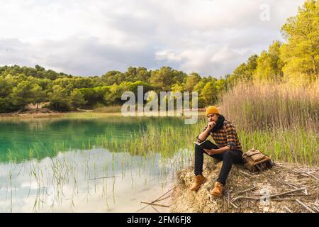 Spanish traveler enjoying reading a book sitting on a peaceful lake Stock Photo