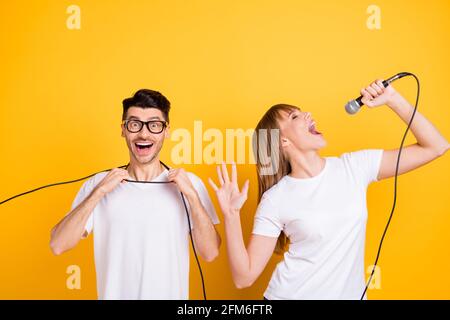 Photo of sweet pretty two persons dressed white t-shirt glasses singing songs microphone isolated yellow color background Stock Photo