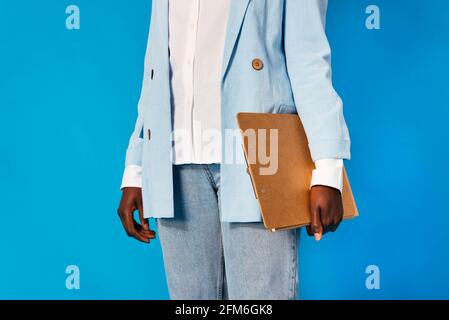 Unrecognizable black woman in trendy jacket and trousers standing against blue background Stock Photo