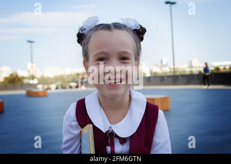 Close-up portrait of adorable little school girl wearing stylish uniform, smiling and laughing outdoors. Back to school concept. Stock Photo