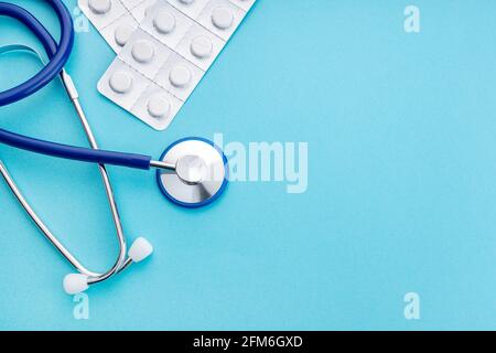 Stethoscope and medicine pills on blue background. Health care or pharmacy concept background. Copy space. Top view Stock Photo