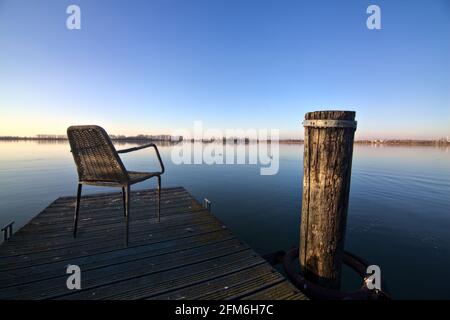 Empty chair on a mooring of a river at sunset in the italian countryside Stock Photo
