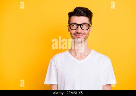 Photo of tricky funny young guy dressed white t-shirt glasses smiling looking empty space isolated yellow color background Stock Photo