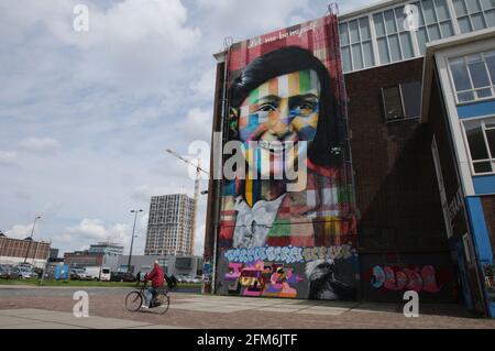 Amsterdam, Netherlands. 06th May, 2021. A man ride bicycle past by giant mural of Anne Frank titled Let me be Myself by Brazilian artist Eduardo Kobra at the former docklands building on May 6, 2020 in Amsterdam, Netherlands. A former shipyard located on the banks of the River IJ in Amsterdam Noord, along with countless murals, artistsÕ residences and studios, the NDSM neighbourhood is famous for graffiti art with new pieces emblazoning sheds and shipping containers almost weekly. (Photo by Paulo Amorim/Sipa USA) Credit: Sipa USA/Alamy Live News Stock Photo