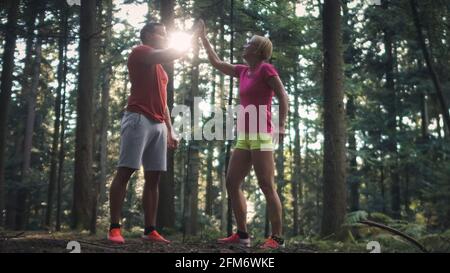 Smiling Caucasian couple in sportswear standing in the forest, giving high five to each other Stock Photo