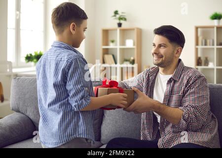 Happy smiling father sitting on sofa taking surprise gift box from son hands Stock Photo