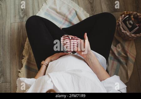 A pregnant woman holding a heart in her hands, a soft toy. Top view. Waiting for a baby. women's happiness Stock Photo