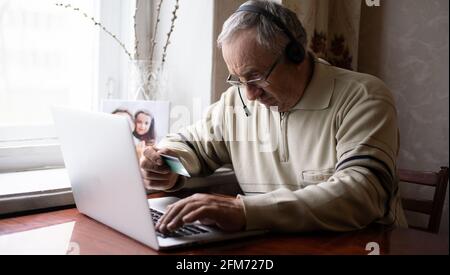 Smiling senior man wear earphones wave to camera having video call on laptop, happy elderly male in headphones sit on couch at home talk using modern Stock Photo
