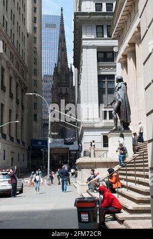 People are sitting in a front of the Federal building on Wall Street, New York. The view on Trinity Church. Stock Photo