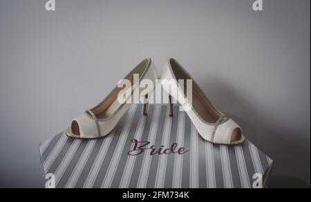 Brides white and silver shoes displayed on a striped hat box saying bride Stock Photo