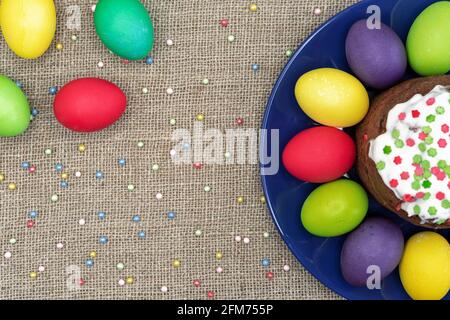 Round plate with multicolored Easter eggs and Easter cake on a burlap background. Stock Photo